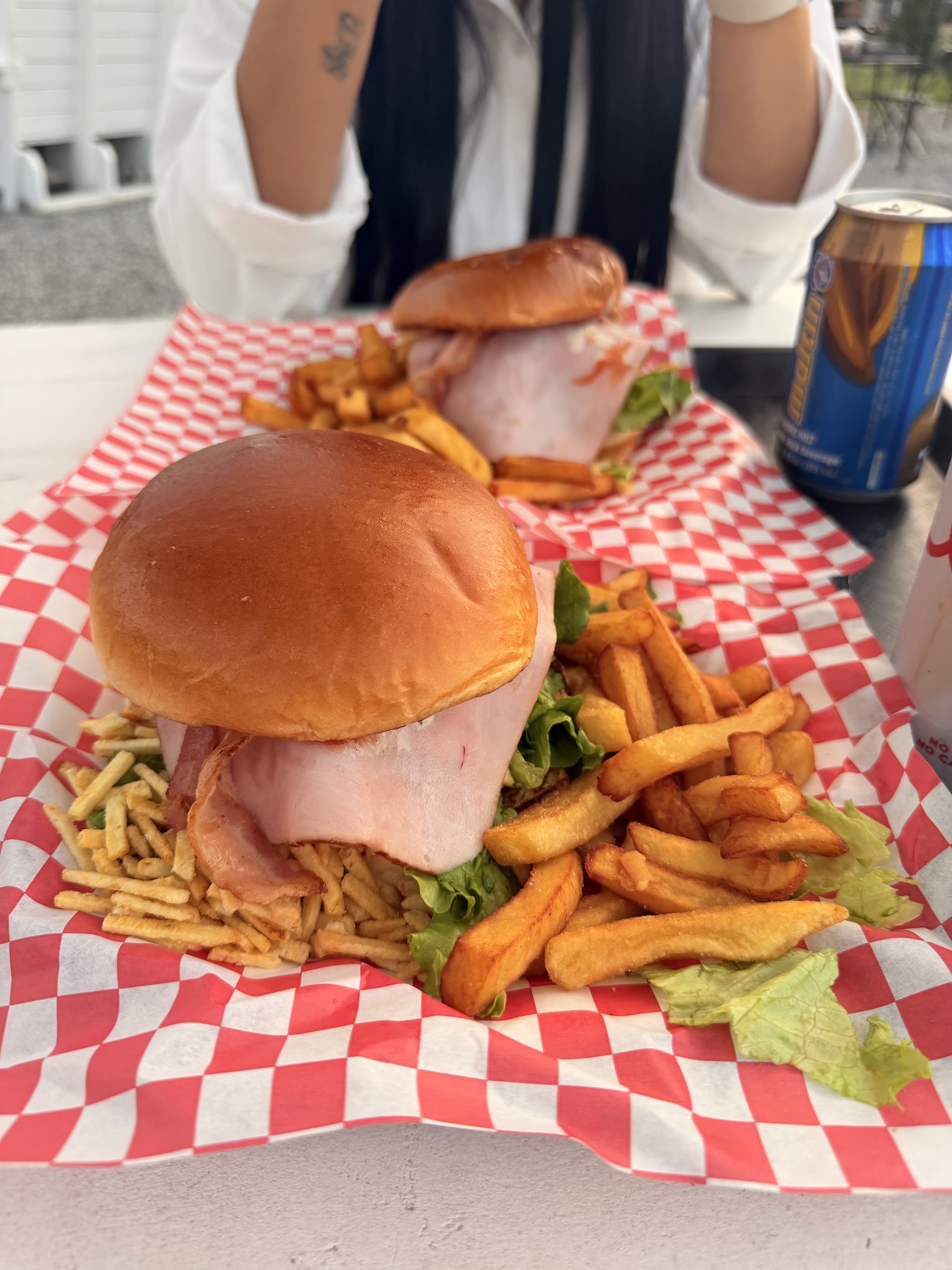A burger piled with ham and bacon, served with fries on red checkered paper