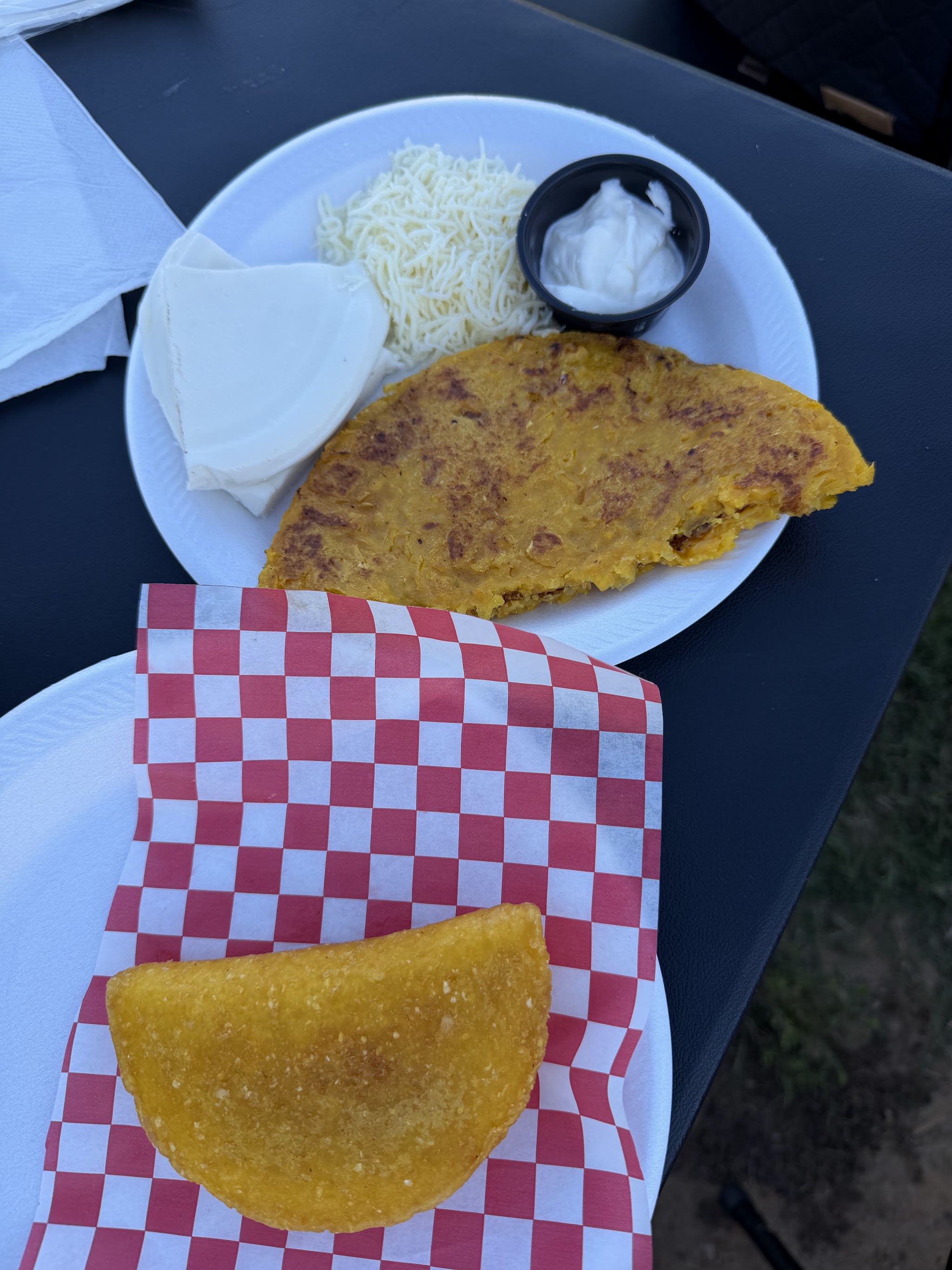 A cachapa with white cheese and a fried corn empanada on red checkered paper